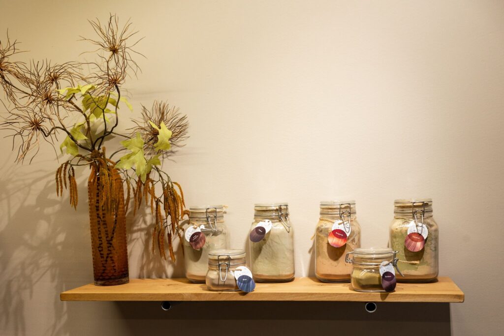 Glazen potten met plantaardige haarverf en droogbloemen op een plank in de salon